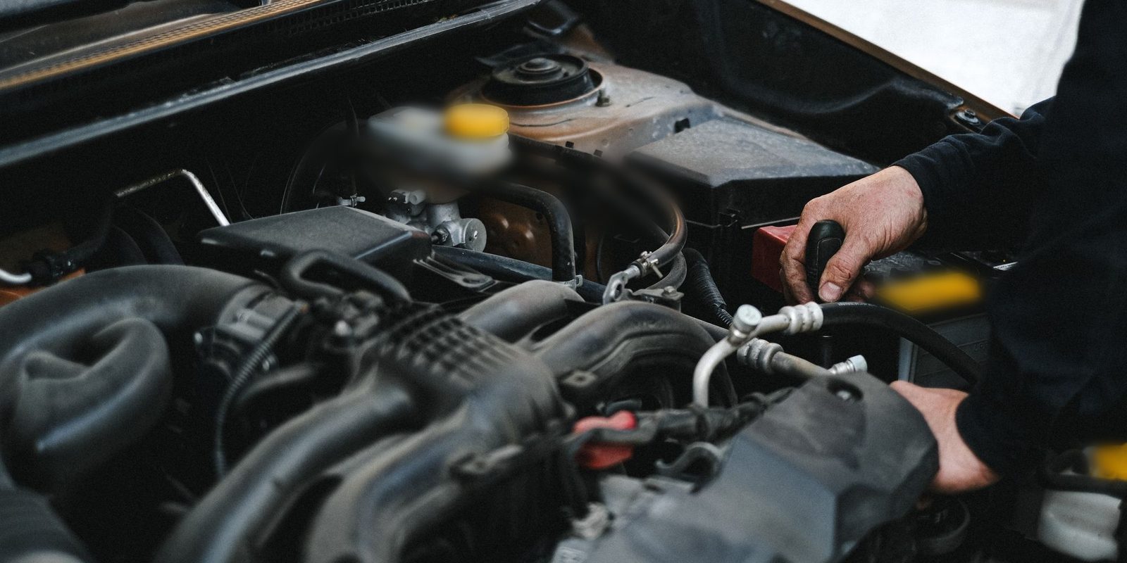 Mãos mexendo no compartimento do motor de um carro com o capô aberto, perto do reservatório de fluido