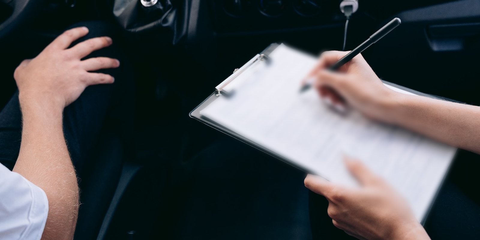 Pessoa preenchendo uma ficha presa a uma prancheta dentro de um carro, ao lado da alavanca de câmbio